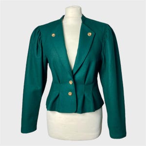 Può includere: Un blazer verde scuro con bottoni dorati. Il blazer ha una vita stretta e un orlo leggermente svasato.
