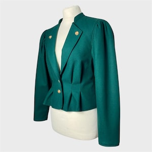 May include: A vintage emerald green blazer with a stand-up collar and gold-colored buttons. The blazer features a tailored fit with pleats at the waist and puffed sleeves. The jacket is displayed on a mannequin.