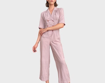 May include: A mauve-colored jumpsuit with a double-breasted button closure, short sleeves, and a relaxed fit.