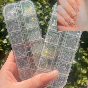 May include: Two clear plastic containers filled with small, clear rhinestones. The containers are labelled with numbers 1 through 10. A hand is holding the containers.