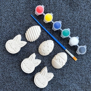 May include: A set of six unpainted ceramic Easter eggs and bunnies, along with a paintbrush and eight small pots of paint in red, yellow, blue, green, white, and black.