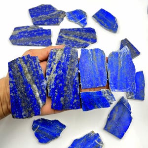 Puede incluir: Un conjunto de piedras de lapislázuli en bruto y pulidas. Las piedras son de color azul intenso con vetas grises y doradas. Se aprecian las formas irregulares y las texturas naturales.