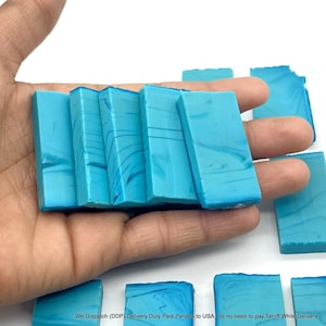 May include: A collection of rectangular turquoise blue stone slabs featuring subtle white marbled veining. The smooth, flat pieces are arranged in a group, with several held in a palm and others resting on a plain white surface, displaying a consistent color.