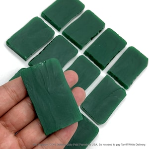 May include: A collection of rectangular dark green wax blocks with a smooth, matte finish. Each piece features slightly irregular, textured edges and a solid, opaque appearance. One block is held in the foreground, displaying a flat surface.