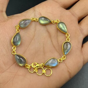 May include: A gold-toned bracelet featuring teardrop-shaped labradorite stones. Each stone is set in a gold bezel and linked together with small gold chain segments. The bracelet has a lobster clasp closure.