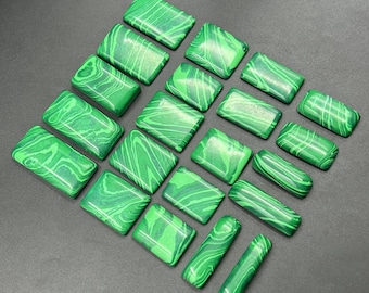 Op de afbeelding: Een verzameling rechthoekige en cilindrische malachietstenen. De stenen zijn heldergroen met donkerdere groene wervelpatronen. De opstelling staat op een donkergrijze ondergrond, met de gepolijste edelstenen.