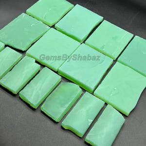 May include: A collection of light green, rectangular and square-shaped gemstones. The gemstones are arranged on a dark surface. The text "GemsByShabaz" is visible on the image.