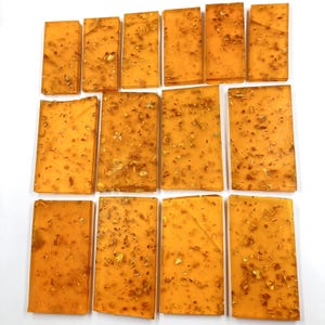 May include: A selection of amber-coloured resin rectangles, each embedded with gold leaf. The pieces are displayed on a white background, highlighting their translucent nature and decorative use. The gold flakes provide a luxurious finish.