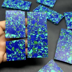 May include: A collection of azurite slabs in various rectangular and square shapes, displaying a deep blue hue with green and white speckles. The slabs are of different sizes and are presented on a dark background, highlighting the natural stone's unique patterns.