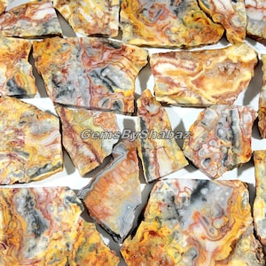 May include: A collection of irregularly shaped, polished gemstones with a variety of colors. The stones feature patterns of yellow, orange, red, gray, and black. The text "GemsByShabaz" is visible on the image.