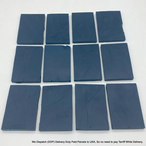 Puede incluir: Doce bloques rectangulares de material azul oscuro dispuestos en tres filas de cuatro. Cada bloque presenta una superficie lisa y mate con sutiles y tenues hendiduras o pliegues lineales en la parte superior, mostrando un aspecto uniforme.