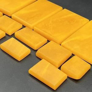 Puede incluir: Una colección de baldosas de piedra de color ámbar de diferentes tamaños, rectangulares y cuadradas. Las baldosas están dispuestas en diagonal, mostrando sus superficies pulidas y sus sutiles vetas. La disposición sugiere un elemento artesanal o de diseño.