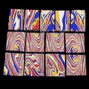 May include: A collection of twelve rectangular blocks with a marbled design. The blocks feature a swirling pattern of red, yellow, blue, and white. The blocks are arranged on a black surface, showcasing the vibrant colors and unique patterns.