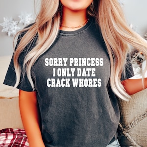 May include: A dark grey t-shirt with the text "SORRY PRINCESS I ONLY DATE CRACK WHORES" printed in white.