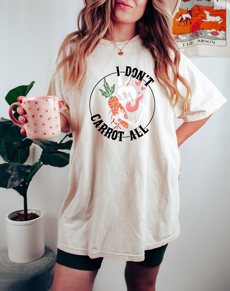 Może przedstawiać: Biały t-shirt z czarnym kołem graficznym przedstawiającym kresk&oacute;wkową marchewkę z czaszką i płomieniami. Wok&oacute;ł grafiki widnieje napis "I Don't Carrot All".