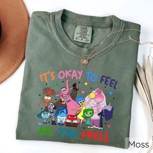 May include: Green t-shirt with a graphic of characters from the movie Inside Out. The text on the shirt reads "It's okay to feel all the feels".