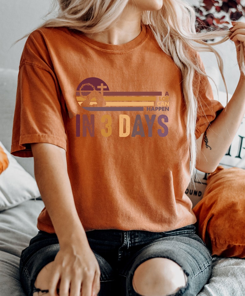 Może przedstawiać: Koszulka w kolorze rdzy z nadrukiem graficznym przedstawiającym krzyż, koronę cierniową i tekst "A lot can happen in 3 days".
