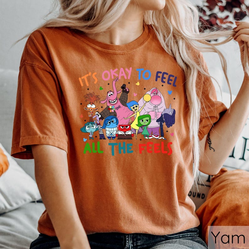 May include: A brown t-shirt with a graphic of characters from the movie Inside Out. The text on the shirt reads "It's okay to feel all the feels."