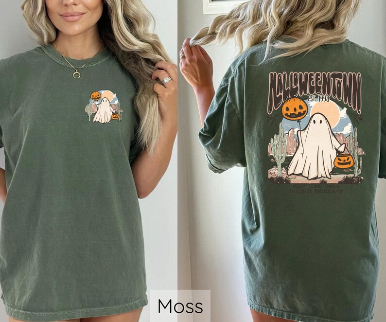 May include: Moss green t-shirt featuring a Halloween-themed graphic. The front graphic shows a ghost with a pumpkin and a desert scene. The back of the shirt displays the text "Halloweentown" with a ghost and pumpkins.