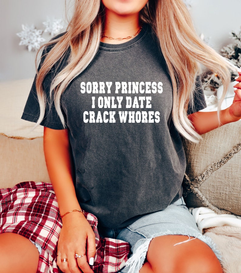 May include: A dark grey t-shirt with the text "SORRY PRINCESS I ONLY DATE CRACK WHORES" printed in white.