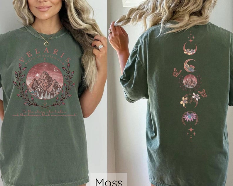 May include: A green t-shirt with a mountain scene and the text "Velaris City of Starlight" on the front. The back of the shirt features a vertical design of moons, flowers, and stars.