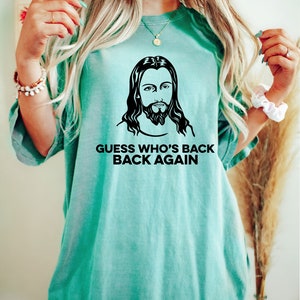 May include: A teal blue t-shirt with a black and white image of Jesus and the text "Guess who's back back again".