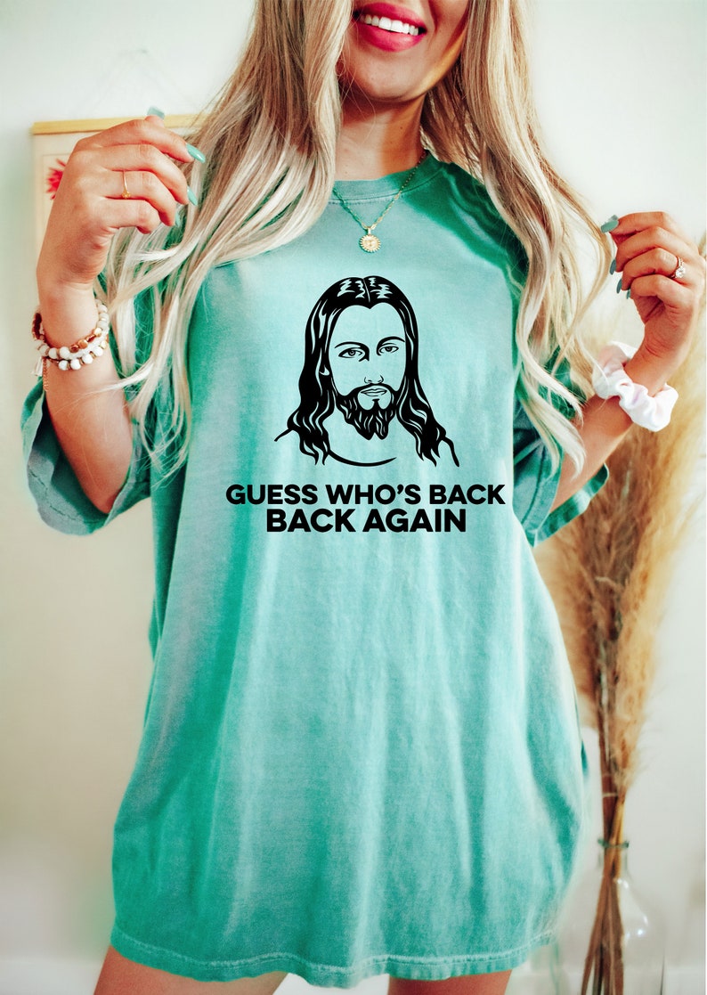 May include: A teal blue t-shirt with a black and white image of Jesus and the text "Guess who's back back again".
