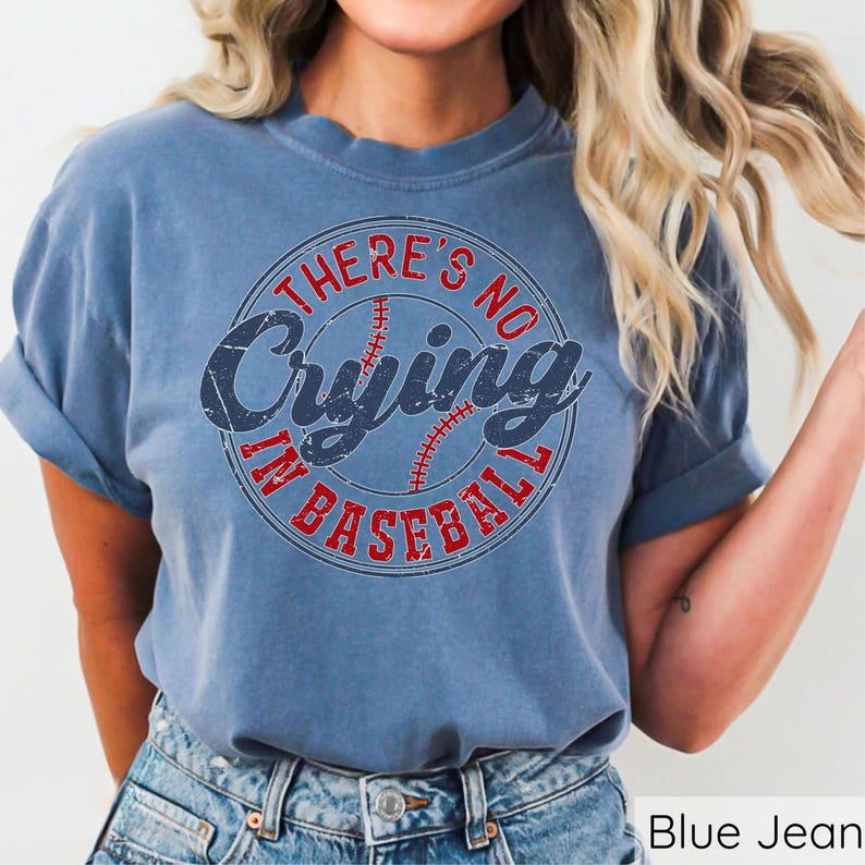 May include: A blue jean t-shirt with a distressed vintage look. The shirt features a red and white baseball graphic with the text "There's No Crying In Baseball".