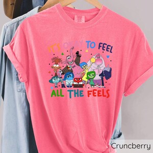 May include: Pink t-shirt with a graphic of characters from the movie Inside Out. The text on the shirt reads "It's okay to feel all the feels."