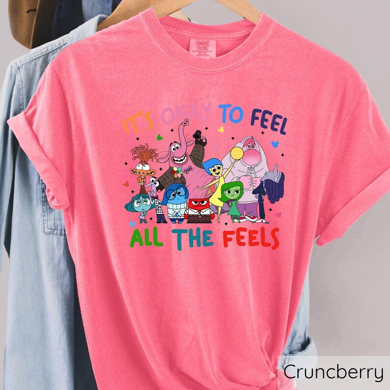 May include: Pink t-shirt with a graphic of characters from the movie Inside Out. The text on the shirt reads "It's okay to feel all the feels."