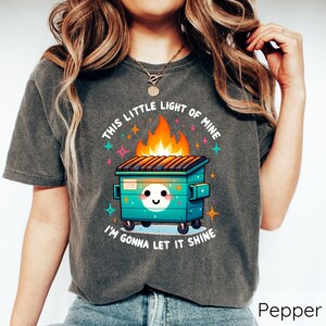 May include: A dark gray t-shirt with a graphic of a cartoon dumpster on fire with the text "This little light of mine I'm gonna let it shine".