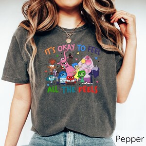 May include: A dark gray t-shirt with a graphic of characters from the movie Inside Out. The text on the shirt reads "It's okay to feel all the feels".
