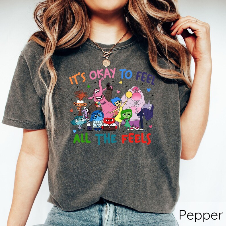 May include: A dark gray t-shirt with a graphic of characters from the movie Inside Out. The text on the shirt reads "It's okay to feel all the feels".