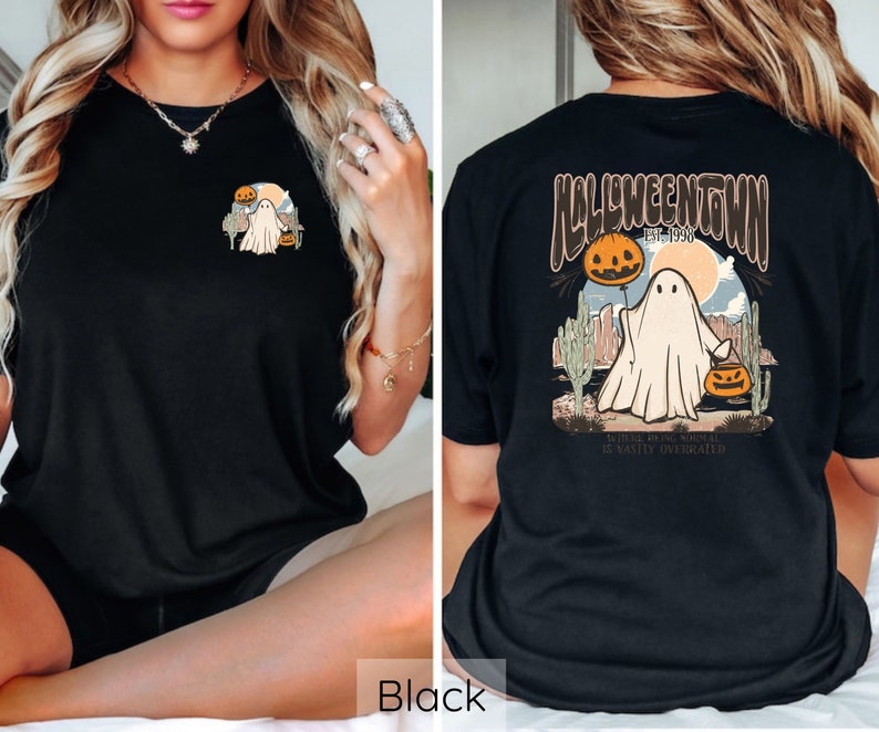 May include: Black t-shirt featuring a Halloween-themed graphic. The front displays a small design of a ghost, pumpkin, and desert landscape. The back showcases a larger design with the text "Halloweentown Est. 1998" and a ghost holding a pumpkin balloon.