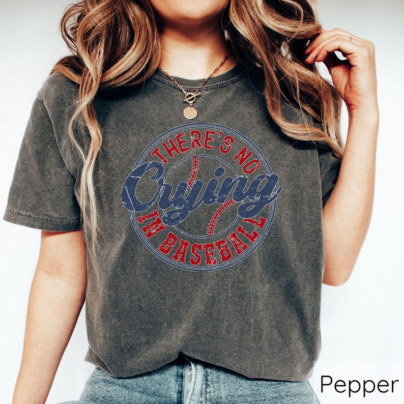 May include: A dark gray t-shirt with a distressed vintage look featuring a baseball graphic and the text "There's No Crying In Baseball".