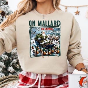 May include: A beige sweatshirt with the text "On Mallard On Gadwall On Canvasback On Pintail" and a graphic of Santa Claus riding a sled pulled by ducks.