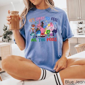 May include: A blue t-shirt with a graphic of characters from the movie Inside Out. The text on the shirt reads "It's okay to feel all the feels."