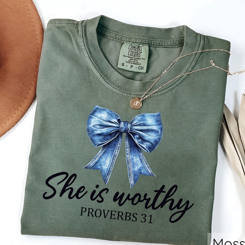 May include: A green t-shirt with a blue denim bow and the text "She is worthy Proverbs 31" printed on the front.