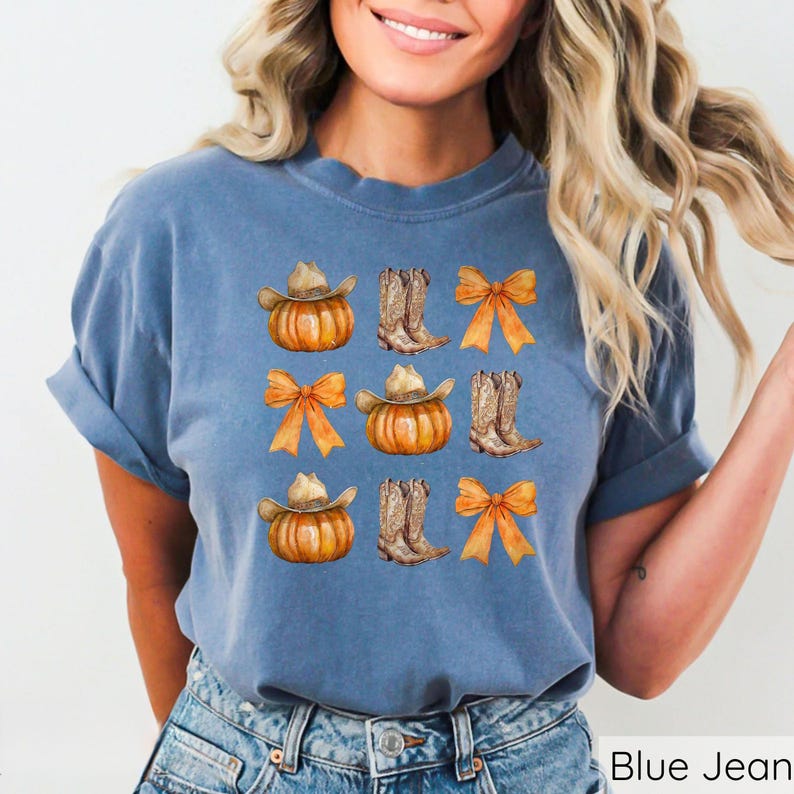 May include: Blue t-shirt with a watercolor design featuring pumpkins wearing cowboy hats, cowboy boots, and orange bows. The shirt is a solid blue color and has rolled-up sleeves. The words "Blue Jean" are printed at the bottom right.