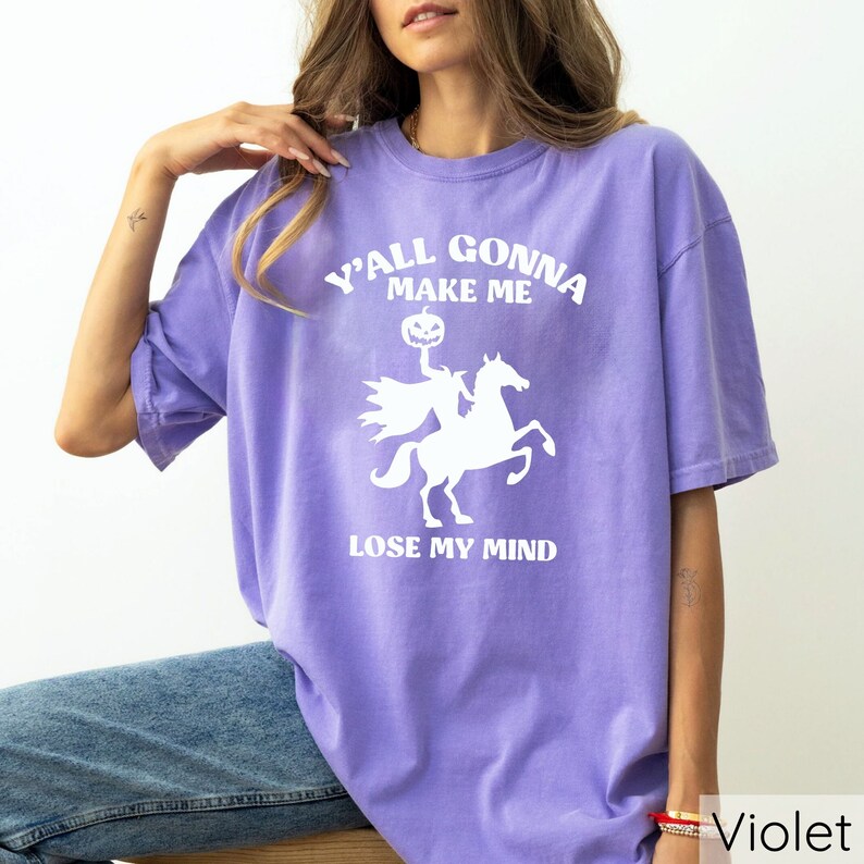 May include: A purple t-shirt with a white graphic of a headless horseman riding a horse and holding a jack-o-lantern. The text on the shirt reads "Y'all gonna make me lose my mind".