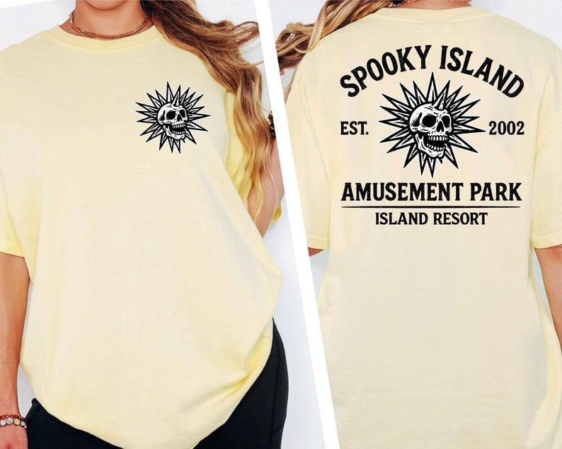 May include: Pale yellow t-shirt featuring a black and white skull graphic with spiky rays on the front and back. The back of the shirt displays the text "SPOOKY ISLAND AMUSEMENT PARK ISLAND RESORT EST. 2002".