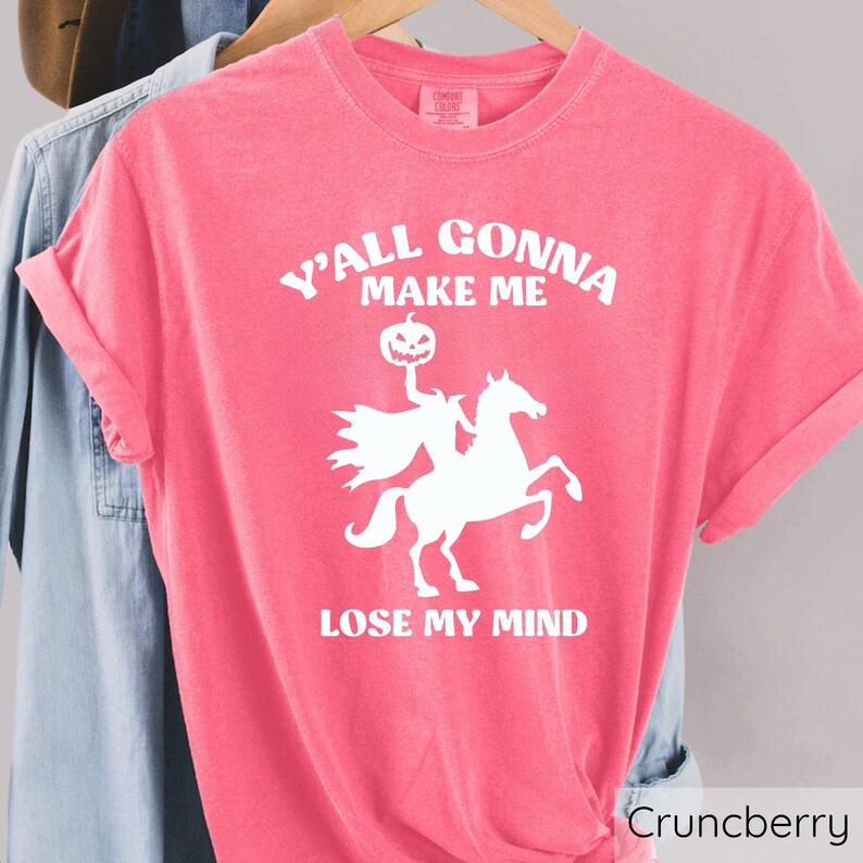 May include: A pink t-shirt with a white graphic of a headless horseman riding a horse and holding a jack-o-lantern. The text on the shirt reads "Y'all gonna make me lose my mind".