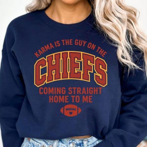 May include: Navy blue sweatshirt with the text "Karma is the Guy on the Chiefs Coming Straight Home to Me." The word "Chiefs" is in a red and gold design, with a football graphic below. A casual top for sports fans.