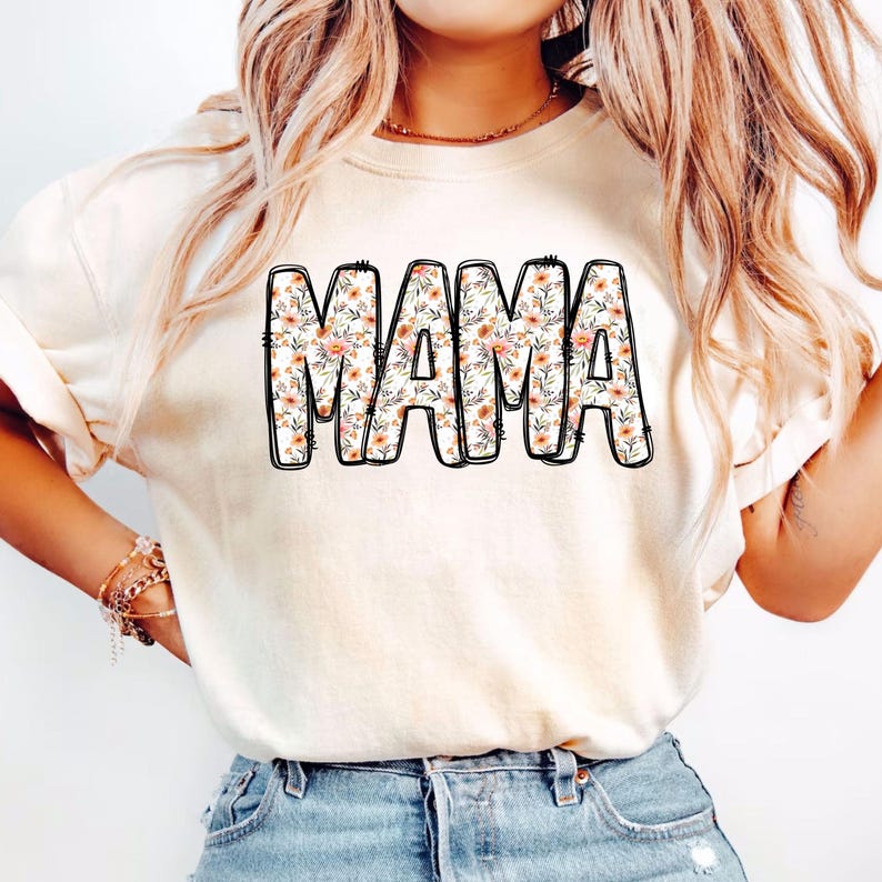 May include: A white t-shirt with a floral print design that says "MAMA" in black outlined letters.