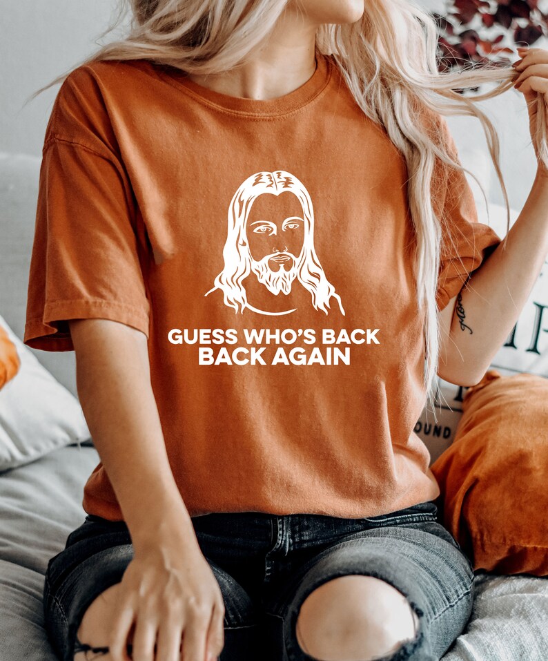 May include: A rust-colored t-shirt with a white graphic of Jesus and the text "GUESS WHO'S BACK BACK AGAIN".