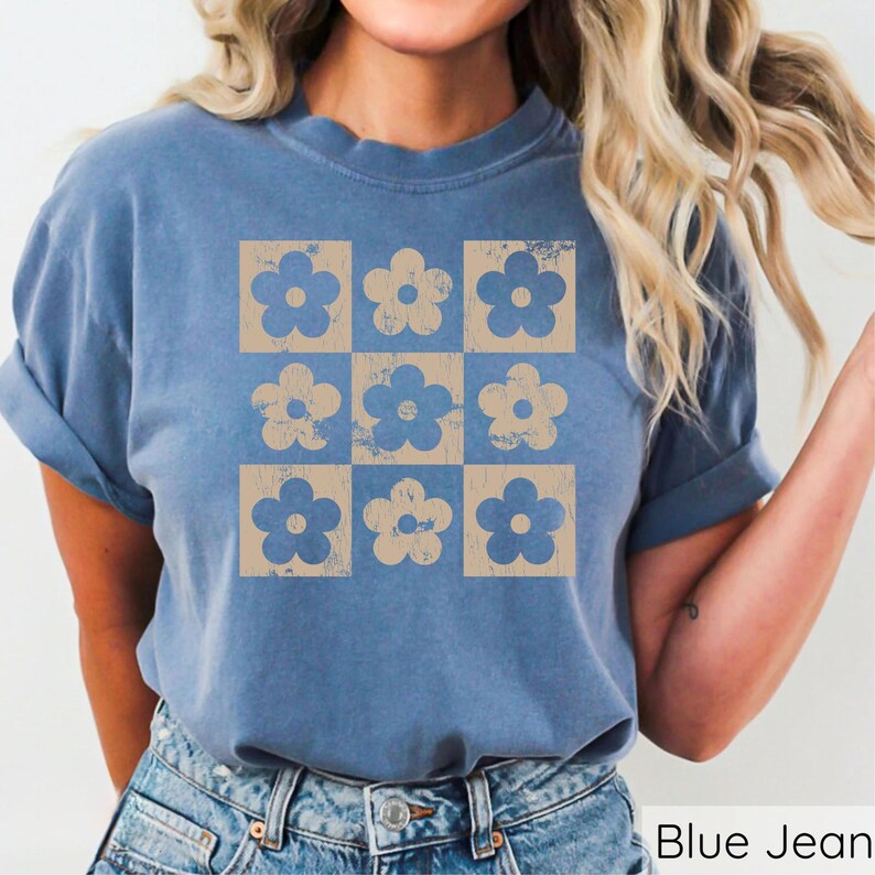 May include: A blue jean t-shirt featuring a vintage-style floral pattern in a light brown colour. The pattern is a grid of nine squares, each containing a stylised flower.