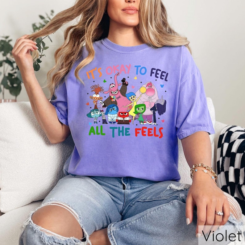 May include: Purple t-shirt with a graphic of characters from the movie Inside Out. The text on the shirt reads "It's okay to feel all the feels."