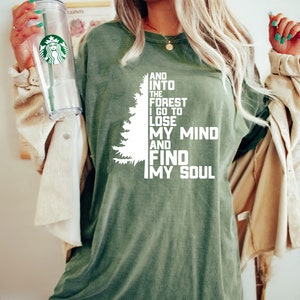K&ouml;nnte beinhalten: Ein gr&uuml;nes T-Shirt mit einer wei&szlig;en Grafik eines Kiefernbaums und dem Text "And into the forest I go to lose my mind and find my soul."