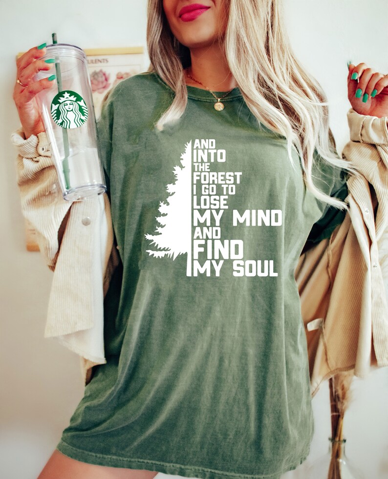 K&ouml;nnte beinhalten: Ein gr&uuml;nes T-Shirt mit einer wei&szlig;en Grafik eines Kiefernbaums und dem Text "And into the forest I go to lose my mind and find my soul."