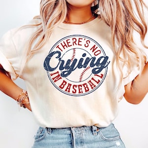 May include: A white t-shirt with a blue and red circle graphic that says "There's No Crying In Baseball".